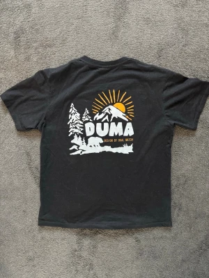 The North Face, Duma  T-shirt - Svart t-shirt från The North Face med liten vit logga på bröstet och stor grafisk print på ryggen med design av DUMA. Storlek L. Tveka inte att kontakta vid frågor, pris kan diskuteras 💯