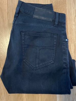Svarta raka jeans tiger of sweden - Säljer ett par svarta jeans med rak passform och klassisk femficksdesign. Jeansen har en diskret läderpatch bak i midjan och är tillverkade i ett mjukt denimtyg. Perfekta för en clean och stilren look. Fråga om mått!!