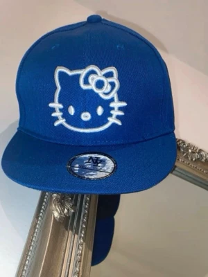 Hello Kitty keps NY New York - Snygg Hello Kitty keps med platt skärm i färgen royal blue. Märkt med NY New York på klistermärket på skärmen. 57.8 cm.