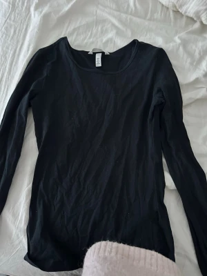 Svart långärmad topp från H&M - En enkel och stilren svart långärmad topp från H&M. Modellen har rund halsringning och är tillverkad i mjuk bomull som sitter bekvämt mot kroppen. Perfekt basplagg att matcha till olika outfits.