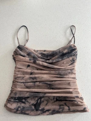 ZARA mesh-topp / linne – XS - Snygg figurnära mesh-topp från Zara i storlek XS. Tunt, stretchigt material, inbyggd korsett med rynkad design som ger en smickrande passform. Beige/brun med mörkare mönster (tie-dye/abstract/åskig look). Smala axelband som går att förlänga/korta ned och  lätt transparent tyg – perfekt till fest, utekväll eller att styla med jeans/kjol. Säljer då den inte passar, knappt använd!