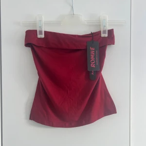 Röd tubtopp  -  Toppen är axelbandslös och har en vikt kant upptill för extra stil. Perfekt att matcha med höga jeans eller kjol för en cool look. 