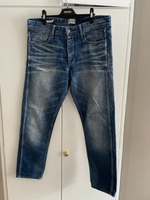 Vintage jeans från Jack and Jones - Säljer ett par blå jeans från Jack and Jones med snygga slitna detaljer och en skön wash. Modellen heter anti fit och skulle säga att de är en rak passform. Hittar ingen storlek men, längd är ca 101 Cm och midjan ca 45 cm. Tveka inte på att höra av dig om du har några frågor.