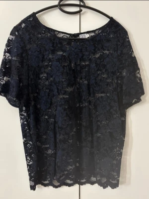 Mörkblå spetsblus från Saint Tropez - Säljer en mörkblå blus från Saint Tropez i genombruten spets med blommigt mönster. Blusen har korta ärmar och rund halsringning. Perfekt att styla med ett linne under för en trendig look.