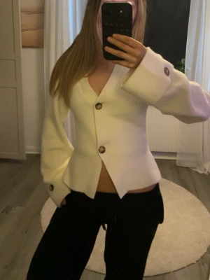 Vit kofta med stora knappar - Trendig vit kofta med stora bruna knappar framtill. Koftan har v-ringning, vida ärmar och breda muddar med knappdetaljer. Perfekt för en stilren och modern look. knappt använd någonting, väldigt bra skick 