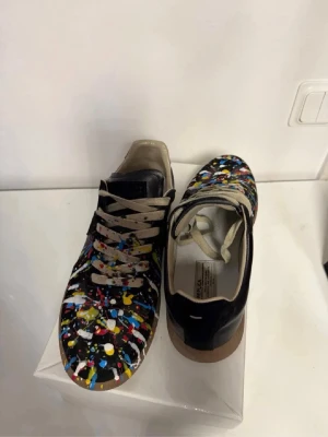 Maison Margiela sneakers med färgstänk - Unika Maison Margiela sneakers i svart läder med färgstänk. Skorna är i mycket bra skick! Hör av dig om du har några frågor osv😁
