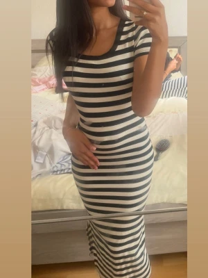 Svartvit randig långklänning - Snygg långklänning med svarta och vita ränder. Klänningen har korta ärmar, rund halsringning och en kroppsnära passform. Den har även en slits på nedre delen av sidan. Klänningen har inga defekter och är nästan helt ny.