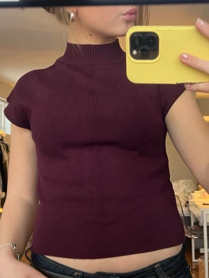 Vinröd polotopp - Säljer en vinröd ribbad polotopp med korta ärmar. Toppen har en hög hals och är figurnära i modellen, perfekt att styla med jeans eller kjol för en trendig outfit🩷