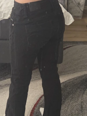 Svarta raka jeans med hög midja - Säljer ett par svarta jeans med rak passform och hög midja. Klassisk femficksmodell med knapp och dragkedja framtill. Jeansen har en stilren look och passar perfekt till många olika outfits. Materialet är denim med lite stretch för extra komfort.