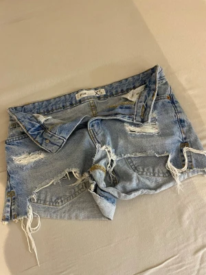 Ljusa slitna jeansshorts XS - Säljer ett par ljusblå jeansshorts från New Yorker i storlek XS. Shortsen har flera slitningar och fransiga kanter. 
