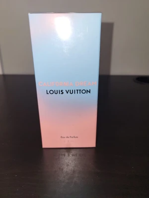 Louis Vuitton California Dream parfym 50 ml - Louis Vuitton California Dream Eau de Parfum i en snygg förpackning med mjuka blå och rosa toner. Lådan har en stilren design med Louis Vuitton-loggan på toppen och text i svart och korallrosa framtill. Lyxig parfym som verkligen sticker ut i badrumshyllan.
