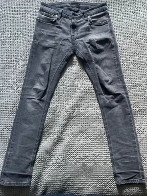 Gråa nudie jeans  - Gråa nudie jeans i 29/30. Snygg tvätt och slitningar med en lagning som ger karaktär. Det finns en röd fläck som man knappt tänker på under den högre framfickan.