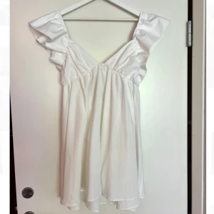 Studentklänning  - Super fin vit klänning med volangärmar och v-ringning. Klänningen har en fin knytdetalj i ryggen och är perfekt till student och sommar. Helt oanvänd, hade den som ”reserv klänning” till min student men behövde aldrig komma till användning