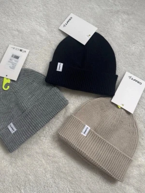 Ribbstickade mössor från Craft - Säljer stilrena ribbstickade mössor från Craft i tre färger: svart, grå och beige. Mössorna har uppvikt kant och diskret logotypmärke framtill. Perfekta för att hålla värmen och ge en clean look till din outfit.