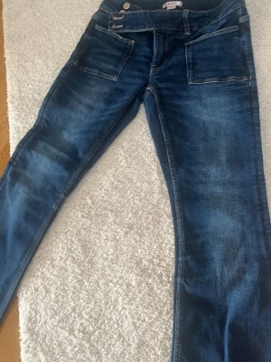 Mörkblå jeans från Gina Tricot - Snygga mörkblå jeans från Gina Tricot med raka ben och stora framfickor. Jeansen har dubbla knappar i midjan och klassisk femficksdesign. Materialet är denim med lätt tvättad effekt för en cool look.