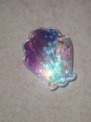 Hårborste - Liten hårborste som är skonsamt mot håret,  formad som en snäcka i regnbågsfärgad plast med glitter och konfetti inuti som inte sitter fast- rör sej när du rör borsten. Perfekt att t.ex ha i väskan för att snabbt fixa frisyren.