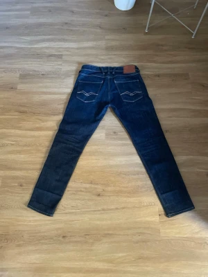 Replay anbass - Säljer ett par mörkblå jeans från Replay med klassisk femficksdesign och kontrastsömmar. Jeansen har raka ben och en snygg läderpatch med Replay-logga bak i midjan. Perfekta för dig som gillar stilrena och tidlösa jeans i slitstarkt denim.