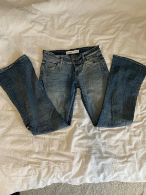 Blå bootcut jeans med låg midja - Säljer ett par blå bootcut jeans från Bershka med klassisk femficksmodell och låg midja. Jeansen har en snygg tvätt med lätt slitning. Säljer pga de inte passar, helt nya