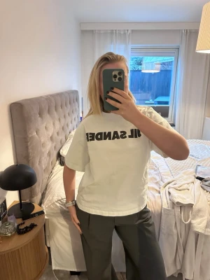 Vit Jil Sander t-shirt med tryck - Vit Jil Sander t-shirt i storlek S, 100 % bomull. Klassisk och stilren modell med tryck – texten är något urtvättad, men i övrigt i mycket bra skick utan fläckar eller hål.  Köpt via Vestiaire Collective och har genomgått deras äkthetskontroll, vilket garanterar originalitet. Plastpåse medföljer. Nypris 4215 kr.  Perfekt basplagg till både vardag och minimalistiska looks 🤍