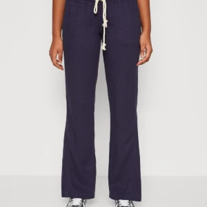 Mörkblå linnebyxor med snörning - Snygga mörkblå linnebyxor med raka ben, låg midja och vit snörning i midjan. Byxorna har resår i midjan, två stora fickor framtill och en avslappnad passform. Perfekta för en chill och stilren look. Använda ca 3 gånger, 599kr nypris. 