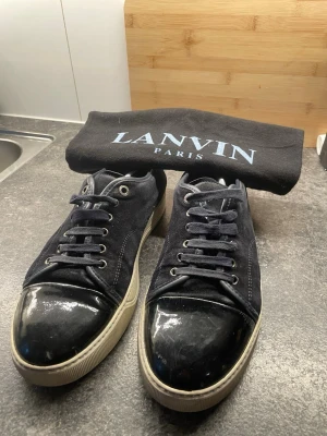 Mörkblå lanvin 41 - Snygga mörkblåa sneakers med ovandel i mocka och en glansig, lackad tå. Skorna har vita sulor och klassisk snörning. Perfekta för dig som gillar en stilren men ändå unik look. Storlek 41 