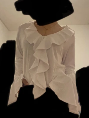 Vit blus med volang och knytband - Säljer en vit blus med stora volanger längs halsringningen och framtill. Blusen har långa ärmar och knytband i ryggen. Storlek M men känns mer som XS/S !! 💘