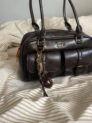 Mörkbrun väska  - Så snygg mörkbrun väska! Kommer med en nyckelring. Rymlig med ett fack med dragkedja på insidan. I väldigt fint skick! 