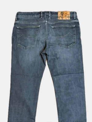 Gråblå jeans från Jacob Cohën - Snygga gråblå jeans från Jacob Cohën med klassisk femficksmodell och raka ben. Jeansen har kontrastsömmar och patch med logga bak i midjan. Tillverkade i mjukt denimtyg som ger en skön känsla och stilren look.