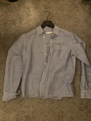 Blårandig skjorta från Zara - Säljer en klassisk blårandig skjorta från Zara i storlek S. Skjortan har vita knappar, bröstficka och lång ärm. Tillverkad i ett lätt och luftigt bomullsmaterial som passar perfekt till vardagslooken.