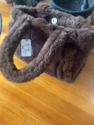 Brun fluffig handväska So Cute - Säljer en brun fluffig handväska från So Cute. Väskan har en mjuk, pälsliknande yta och breda handtag. Stängs med magnetknapp och har en rymlig form. Perfekt accessoar för dig som vill sticka ut med en mysig och trendig look.