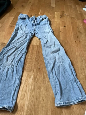 Ljusblå wide leg jeans från H&M - Säljer ett par ljusblå jeans från H&M med wide leg och hög midja. Jeansen har justerbar midja och klassisk femficksdesign. Perfekta för dig som gillar en avslappnad och trendig look.
