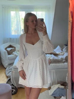 Vit kort klänning med öppen rygg - Supersöt vit kortklänning med broderade detaljer, v-ringning och långa puffärmar. Klänningen har öppen rygg med snörning och knyt i nacken samt i midjan. Perfekt för sommarens alla tillfällen och ger en romantisk vibe. Passar även bra till studenten som jag hade den till!