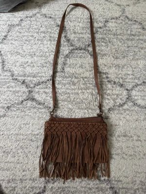 Brun Mocka Väska Indiska  - Säljer en brun axelväska i mocka med fransar och är från märket Indiska. Mycket fint skick och har inga skador eller andra defekter. 