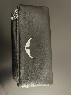 Svart handväska från Zadig & Voltaire - Snygg svart handväska i präg­lat konstläder med silverfärgad kedja och dragkedja från Zadig och voltaire 