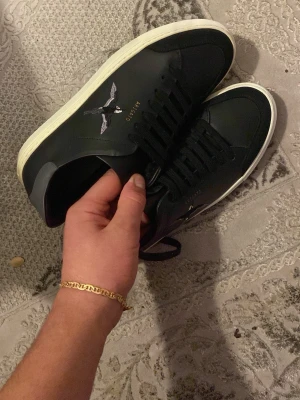 Svarta Kenzo sneakers med broderi - Snygga svarta Kenzo sneakers i läder med vit sula och svart snörning. På sidan finns ett broderat motiv av en flygande fågel och Kenzo-loggan i guld. Klassisk låg modell som passar till det mesta och ger en clean look.