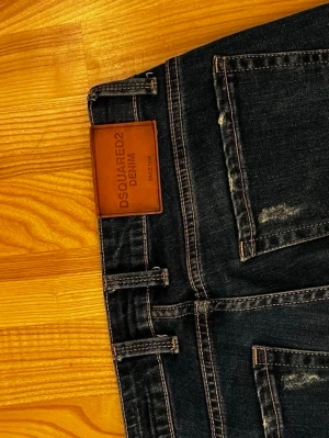 Mörkblå Dsquared2 jeans - Snygga mörkblå jeans från Dsquared2 med slitna detaljer och klassisk femficksmodell. Jeansen har kontrastsömmar och en läderpatch med logga bak i midjan. Perfekta för dig som gillar streetwear och vill ha en trendig look.