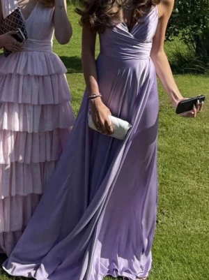 Ljuslila balklänning med v-ringning - Ljus lila satin balklänning från L&S, endast använd på min bal, kemtvättad efteråt. Klänningen är lång och når ner till marken även med klackar. Ny pris 3000, storleken är en längre xs/s