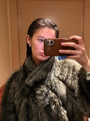 Gråbrun fuskpälsjacka med krage - Säljer en fluffig gråbrun fuskpälsjacka med bred krage och långa ärmar. Jackan har en oversized passform och stängs framtill. Perfekt för dig som vill ha en statementjacka till vintern.