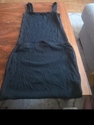 Svart ribbad klänning med smala axelband - Säljer en svart ribbad klänning med smala axelband. Klänningen har en kroppsnära passform och är i kort modell, perfekt för en trendig och enkel look. Materialet är mjukt och stretchigt för extra komfort.