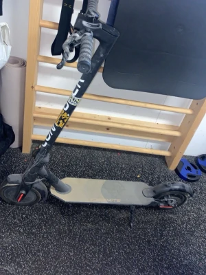 Svart elsparkcykel med dekaler - Säljer en svart elsparkcykel med vita och gula dekaler på styret. Modellen har handbroms, stora hjul och en bred ståplatta. Perfekt för att ta sig runt i stan på ett smidigt sätt. Laddare ingår ej.