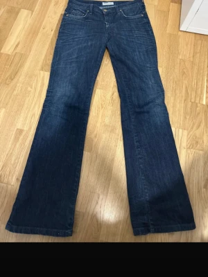 Mörkblå bootcut jeans - Snygga mörkblå bootcut jeans med klassisk femficksmodell och låg midja. Jeansen har en lätt utsvängd passform från knät och ner, vilket ger en retroinspirerad look. Tillverkade i denim med subtila slitningar för en avslappnad vibe.