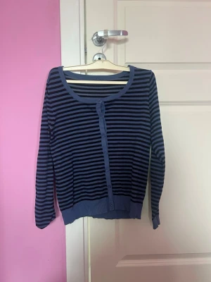 Blå- och svart-randig kofta - Randig kofta i blått och svart med rund halsringning och knäppning framtill. Långa ärmar och ribbade muddar vid ärmslut och nederkant. Perfekt för lager på lager och enkel att matcha med olika outfits.