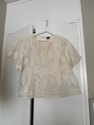 Vit blommig spetsblus från Gina tricot - Säljer en luftig vit spetsblus från gina tricot med korta ärmar och blommigt mönster. Blusen har dekorativa sömmar och transparenta partier som ger en romantisk vibe. Perfekt till jeans eller kjol för en trendig look.