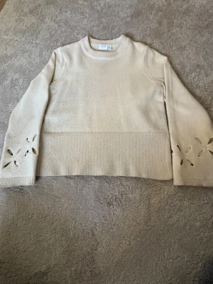Beige stickad tröja med hålmönster - Snygg beige stickad tröja från vila med rund halsringning och långa ärmar. Tröjan har bred ribbad kant nedtill och dekorativa hålmönster i form av blommor på ärmarna. Perfekt för dig som gillar stilrena plagg med en twist.Skriv privat för fler bilder🤗