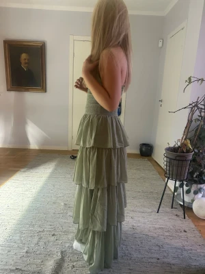 Ljusgrön balklänning - Säljer en ljusgrön långklänning med flera lager volanger och smock i midjan. Klänningen har halterneck och en liten öppning framtill. Perfekt till en bal! Inte använda någon gång då den är lite för stor för mig💞