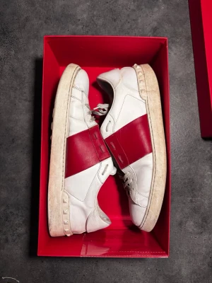 Valentino Garavani Open - Säljer ett par snygga sneakers från Valentino Garavani i vitt läder med bred röd diagonal detalj på sidan. Kommer i originalkartong med dustbag. Pris kan diskutera vid snabb affär ✅