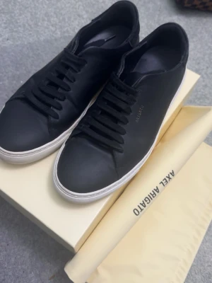Svarta Axel Arigato sneakers  - Stilrena svarta sneakers från Axel Arigato i slätt läder med svart snörning och vit sula. Perfekta till soligt väder och väldigt stiliga. Box och allt som låg i den när jag fick hem dem medföljer.Passar 42/43 i storleken.