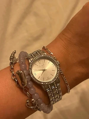 Silver klocka - klocka från regal i silverfärg med metallarmband och gnistrande stenar runt urtavlan och på länken. Aldrig använd.