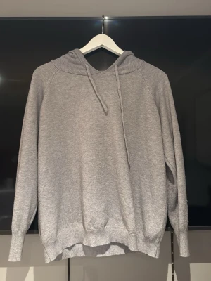 Ljusgrå stickad/casmir hoodie  - En enkel och stilren ljusgrå hoodie med huva. Tillverkad i mjukt material med ribbade muddar vid ärmslut och nederkant. Perfekt för en avslappnad look och passar till det mesta i garderoben.