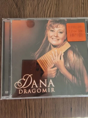 CD Dana Dragomir Panflöjt - CD-skiva med Dana Dragomir där hon framför 16 kända låtar på panflöjt. Omslaget är i plastfodral med ett foto av Dana Dragomir och hennes panflöjt. Låtarna inkluderar bland annat 'Mio min Mio', 'Chiquitita' och 'The Phantom of the Opera'. Perfekt för dig som gillar instrumental musik.